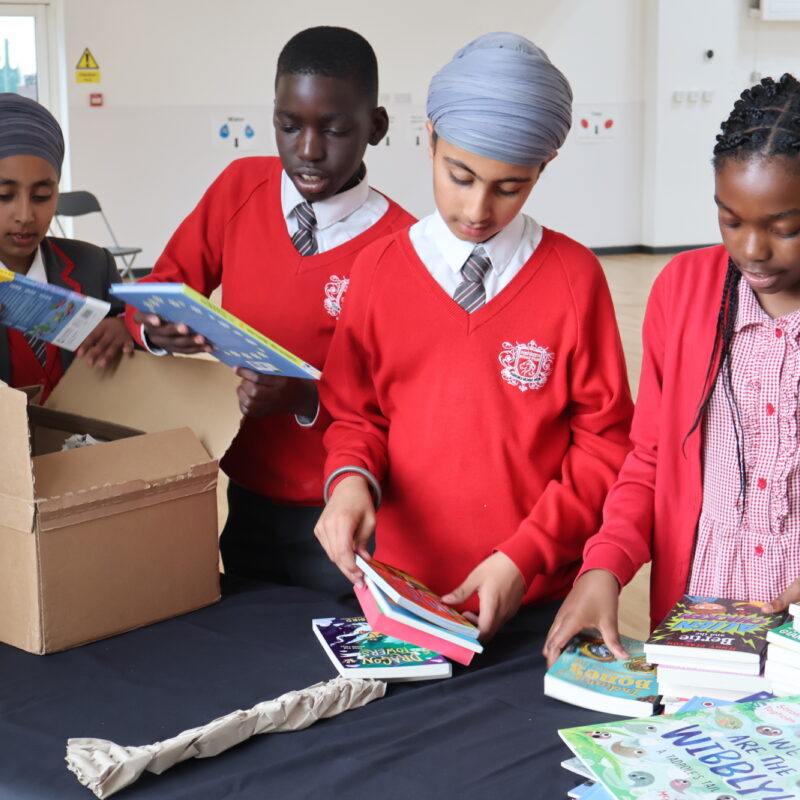 4 children in red school uniform open a box of books