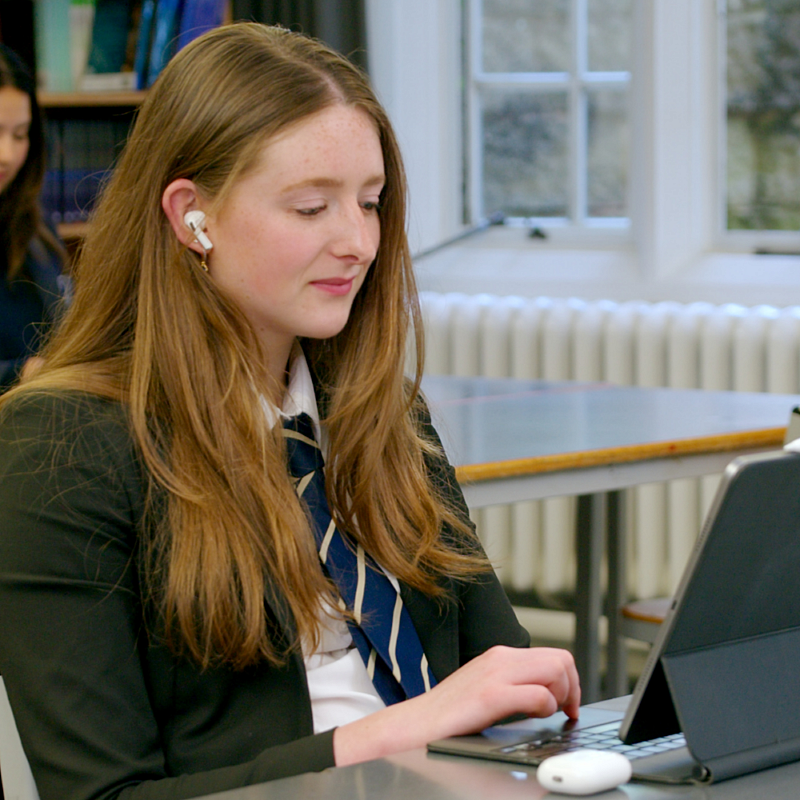 Reading mentor looking at her tablet doing an online reading session with her pupil. She's sat in school uniform in class.