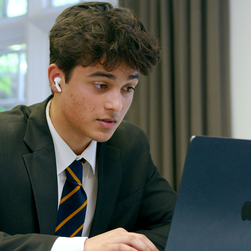 Student on an apple laptop in a reading session wearing school uniform.