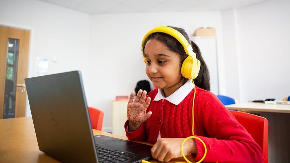 Child in online reading session wearing red uniform and yellow headphones
