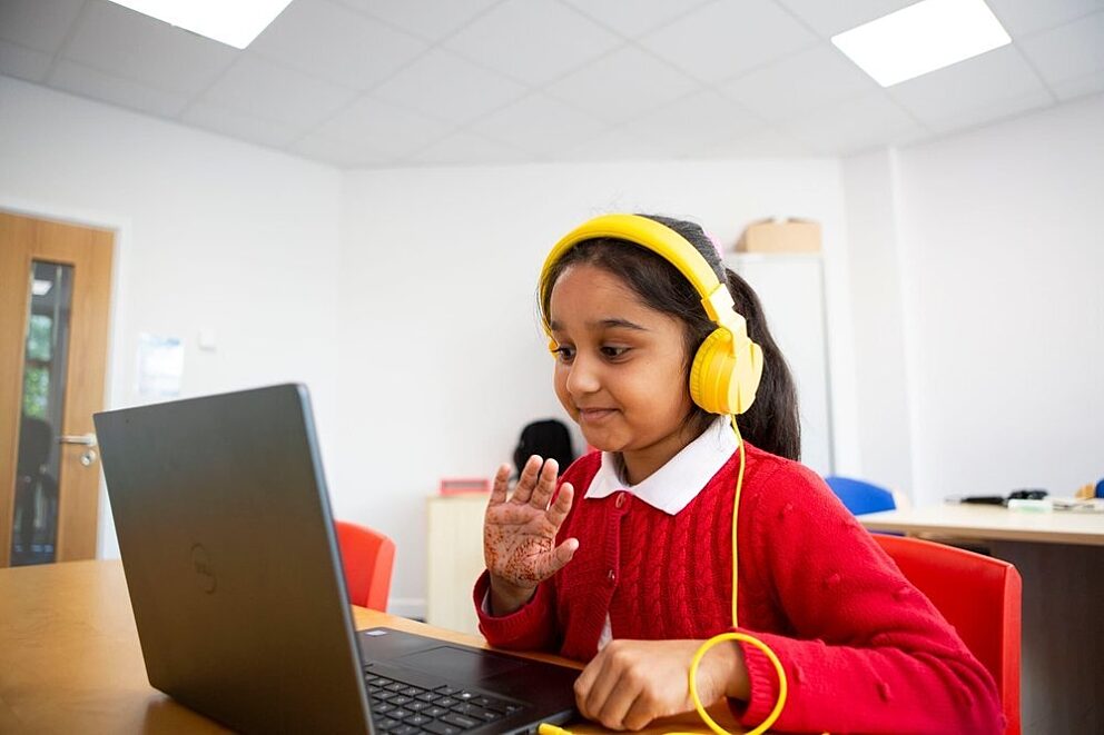 Child in online reading session wearing red uniform and yellow headphones