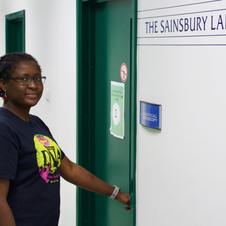 Alice Eseola standing outside the door to the microscopy suite at The Sainsbury Laboratory
