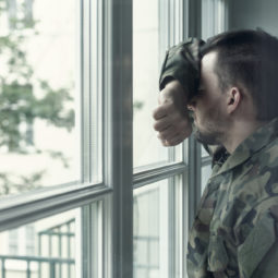 Depressedandsadsoldieringreenuniformwithtraumaafterwarstandingnearthewindow