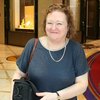 Sheila stands smiling in a hotel foyer with shops in the background